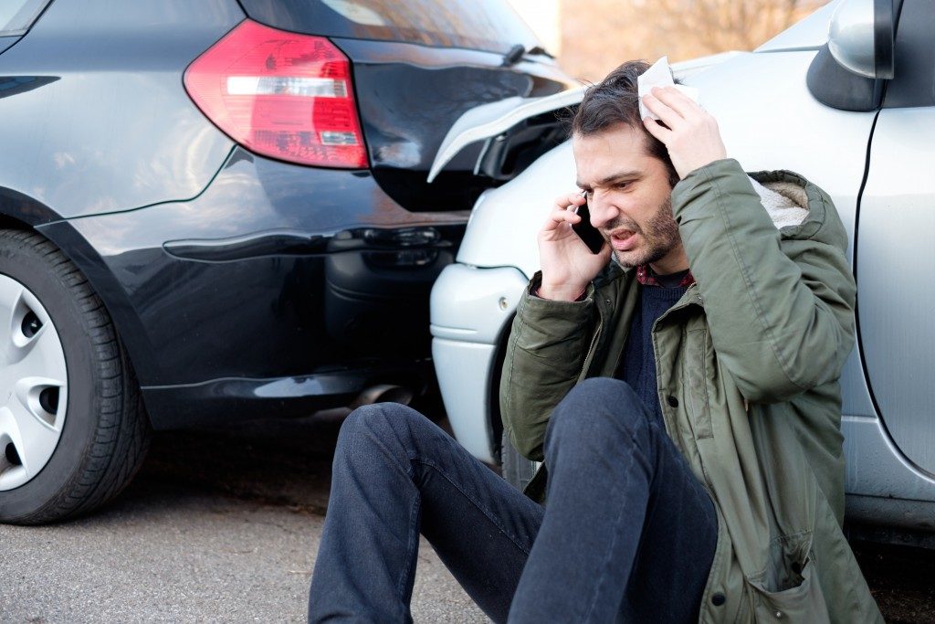 man in an accident sitting beside car