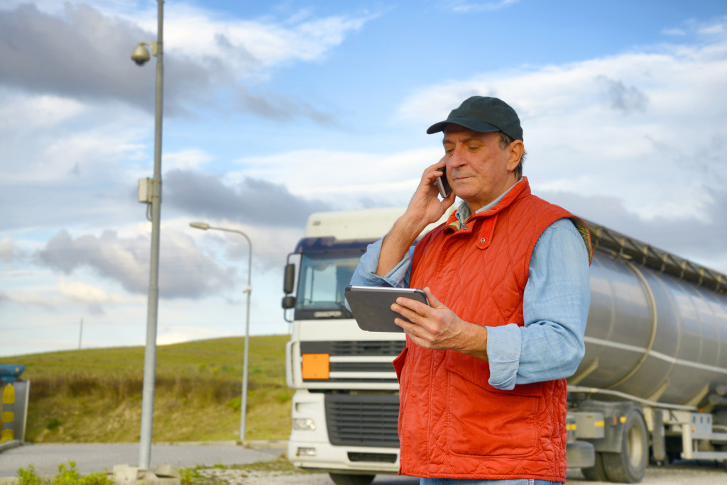 male elderly truck driver using tablet and phone outside parked truck